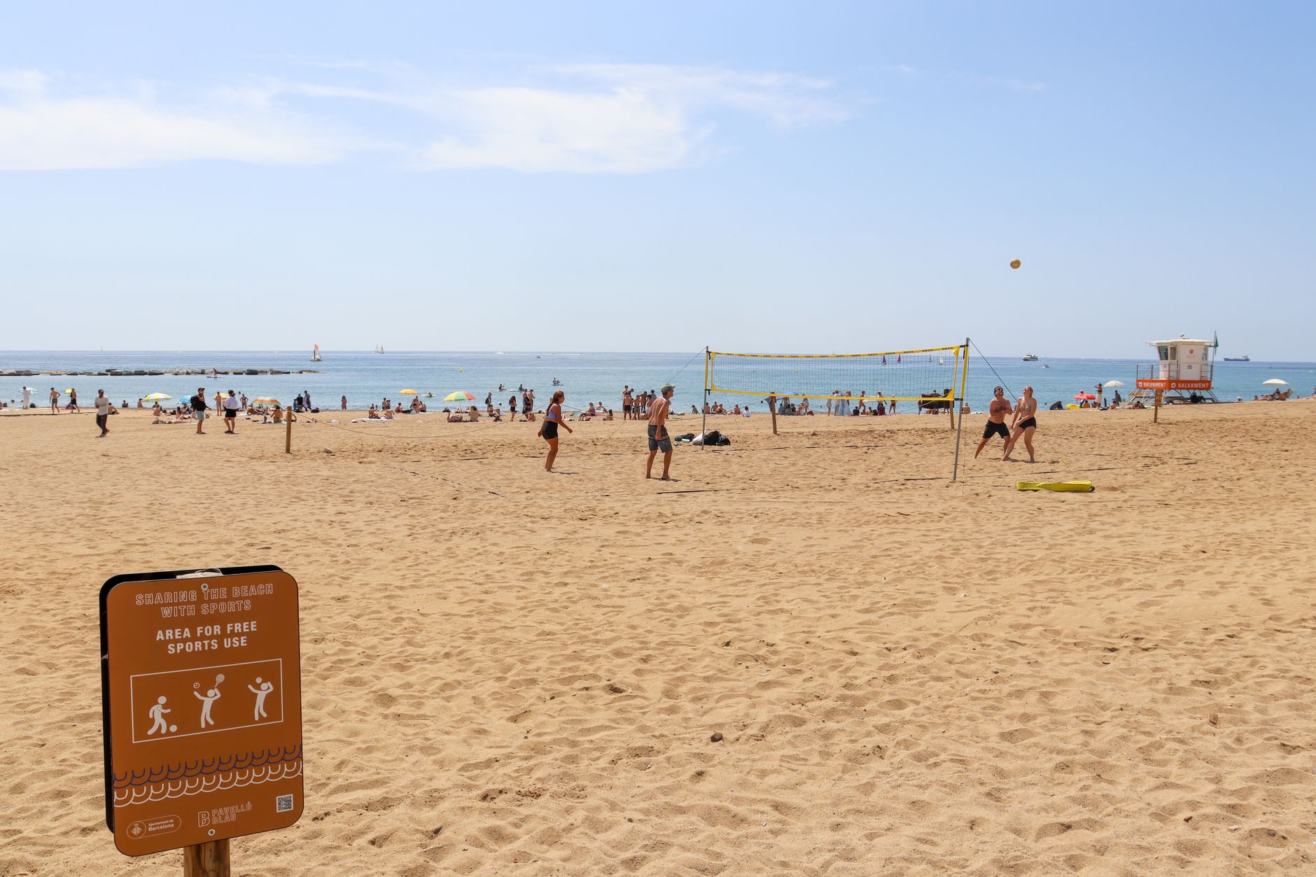People enjoying beach volleyball under sunny skies by the ocean.