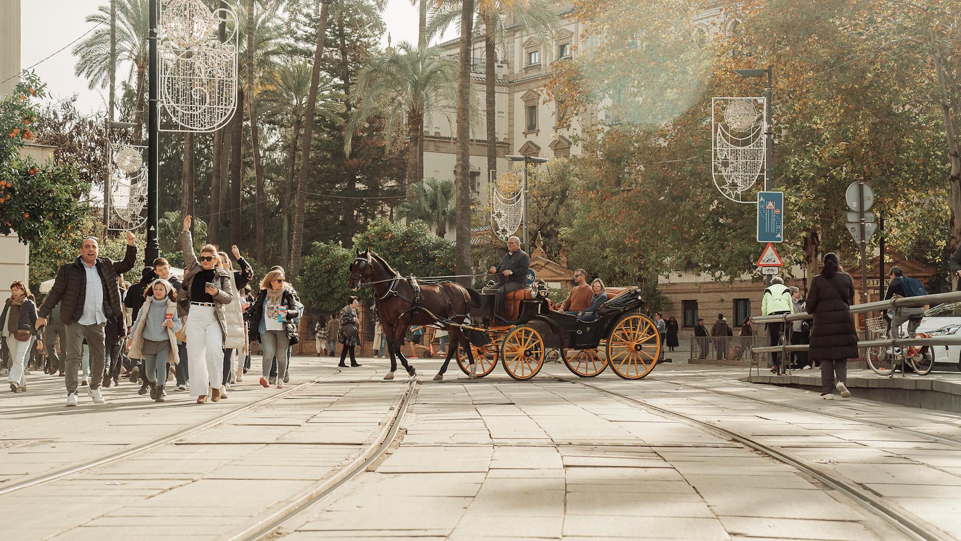 People enjoy a horse carriage ride on a sunny day in Seville, Spain, showcasing lively city life.