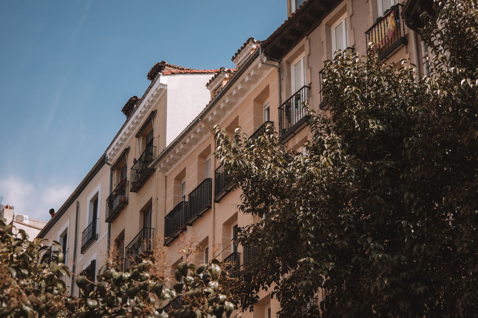 Elegant residential building with balconies and lush trees in Madrid, Spain.