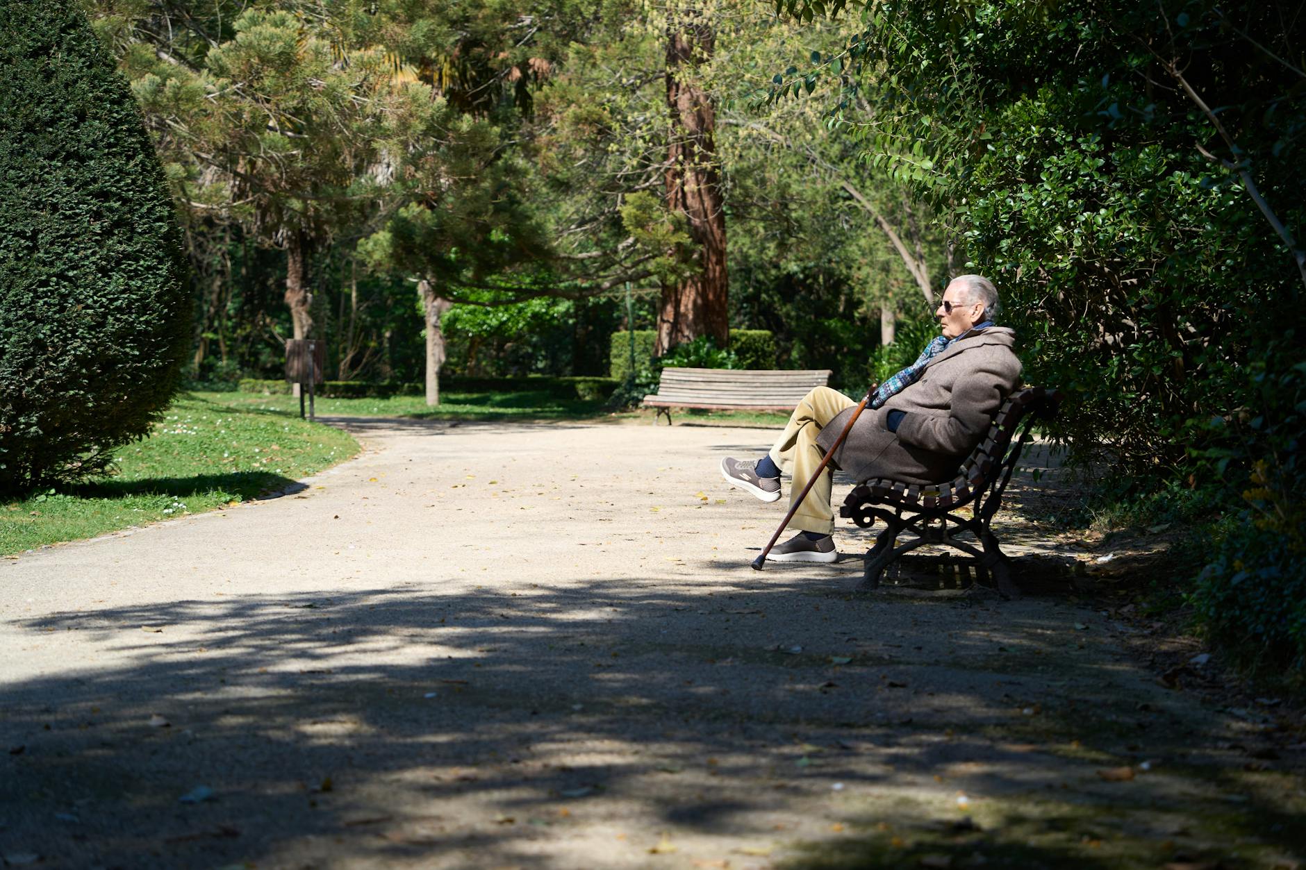 A senior man enjoys a sunny day on a park bench in Valladolid, Spain.