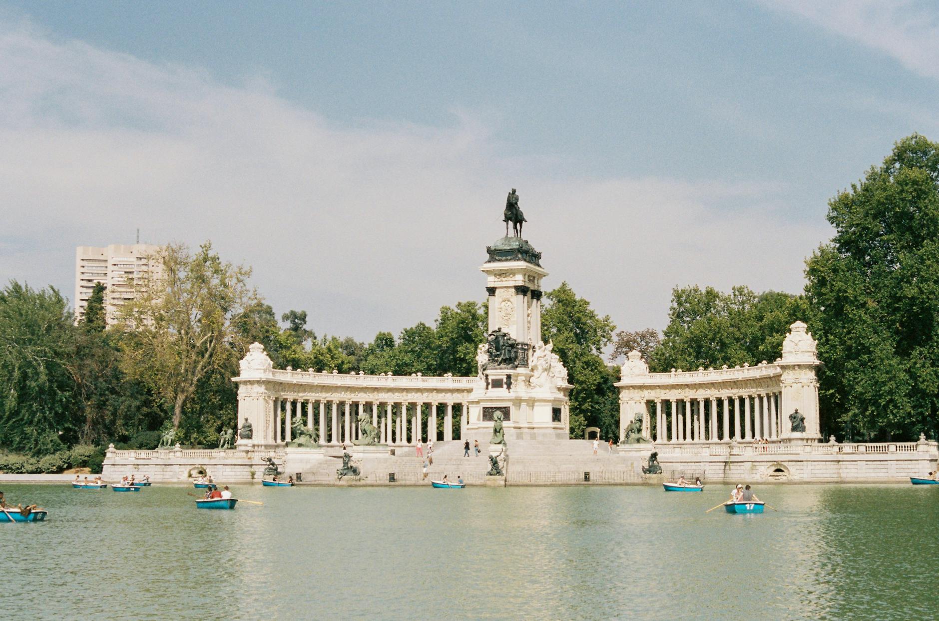 People rowing boats by the Alfonso XII monument in Buen Retiro Park, Madrid, on a sunny day.