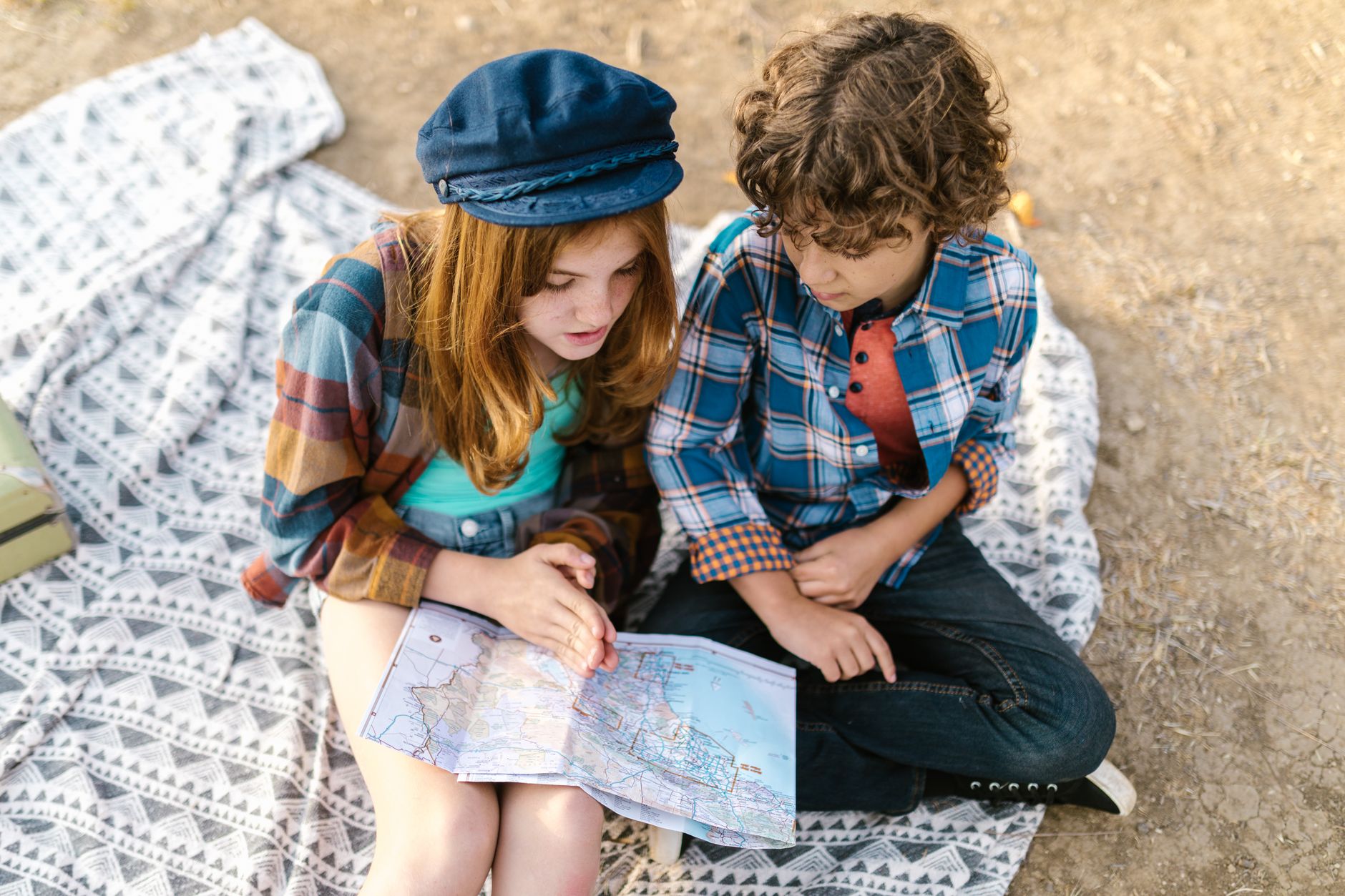 Two children exploring a map while sitting on a picnic blanket outdoors, capturing the essence of adventure and learning.