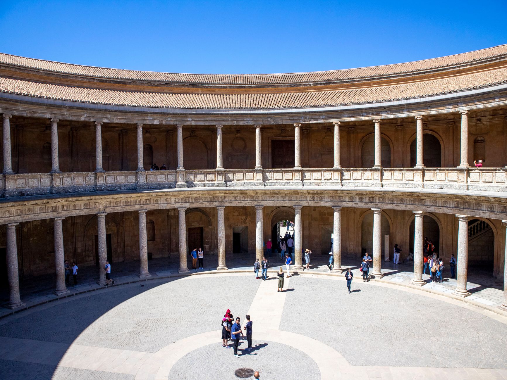 Tourists explore the Renaissance architecture in the circular courtyard of the Palace of Charles V, Granada.