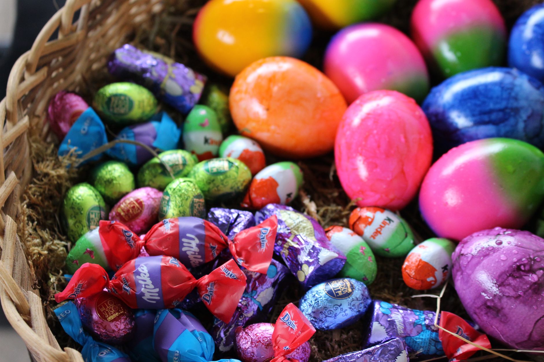 Colorful Easter eggs and wrapped chocolates in a wicker basket for a festive celebration.