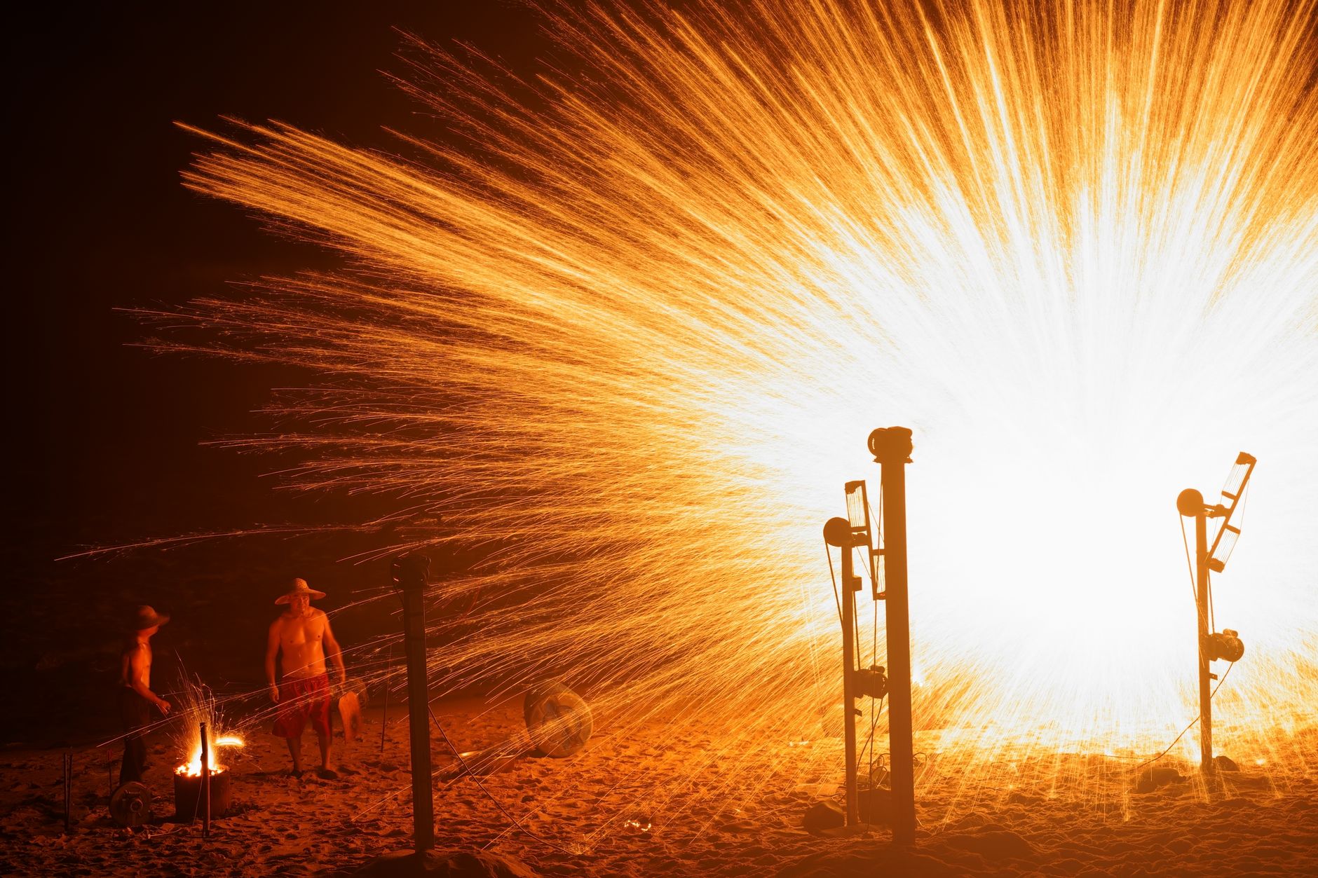 Men enjoy a thrilling fireworks display on a beach at night, creating a dramatic visual spectacle.