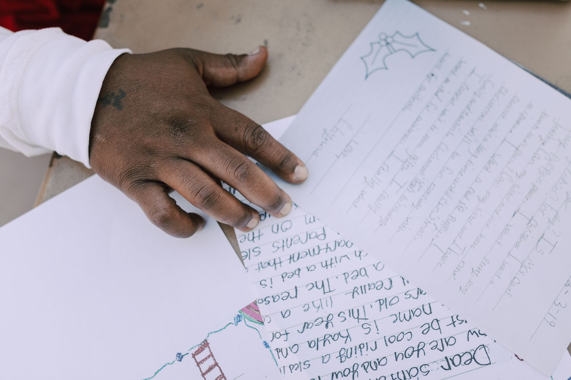 A close-up view of a hand writing a Christmas letter to Santa, featuring holly decorations.
