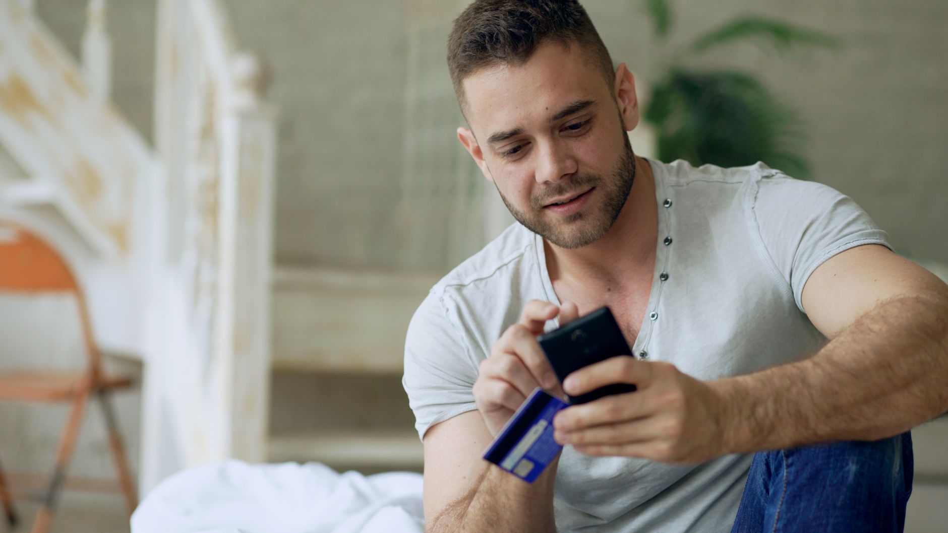 Young man using smartphone and credit card for online shopping indoors.
