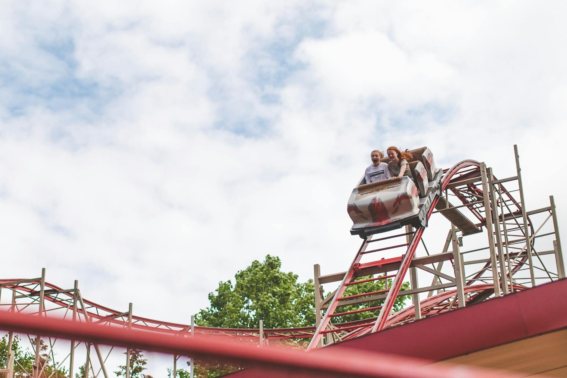 Two happy girls enjoying a thrilling roller coaster ride on a sunny day.