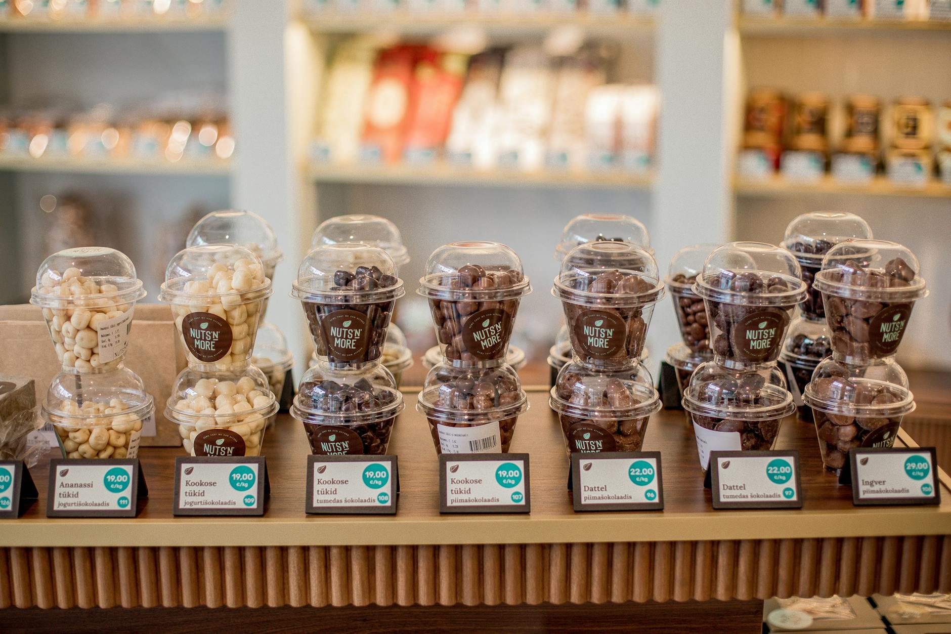 A variety of nuts and snacks in labeled plastic cups on display at a store counter.
