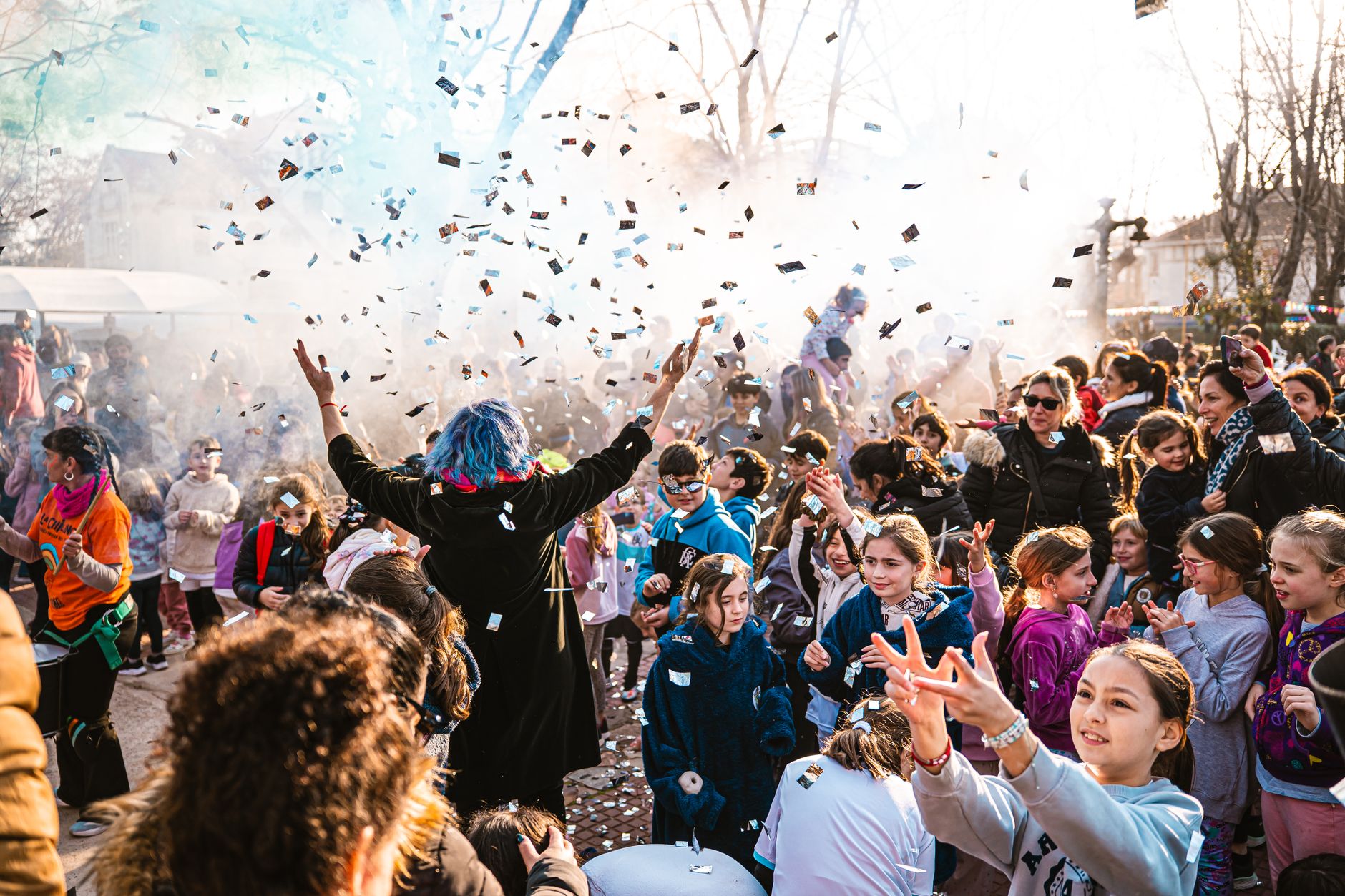A vibrant outdoor celebration with kids enjoying confetti and performers.