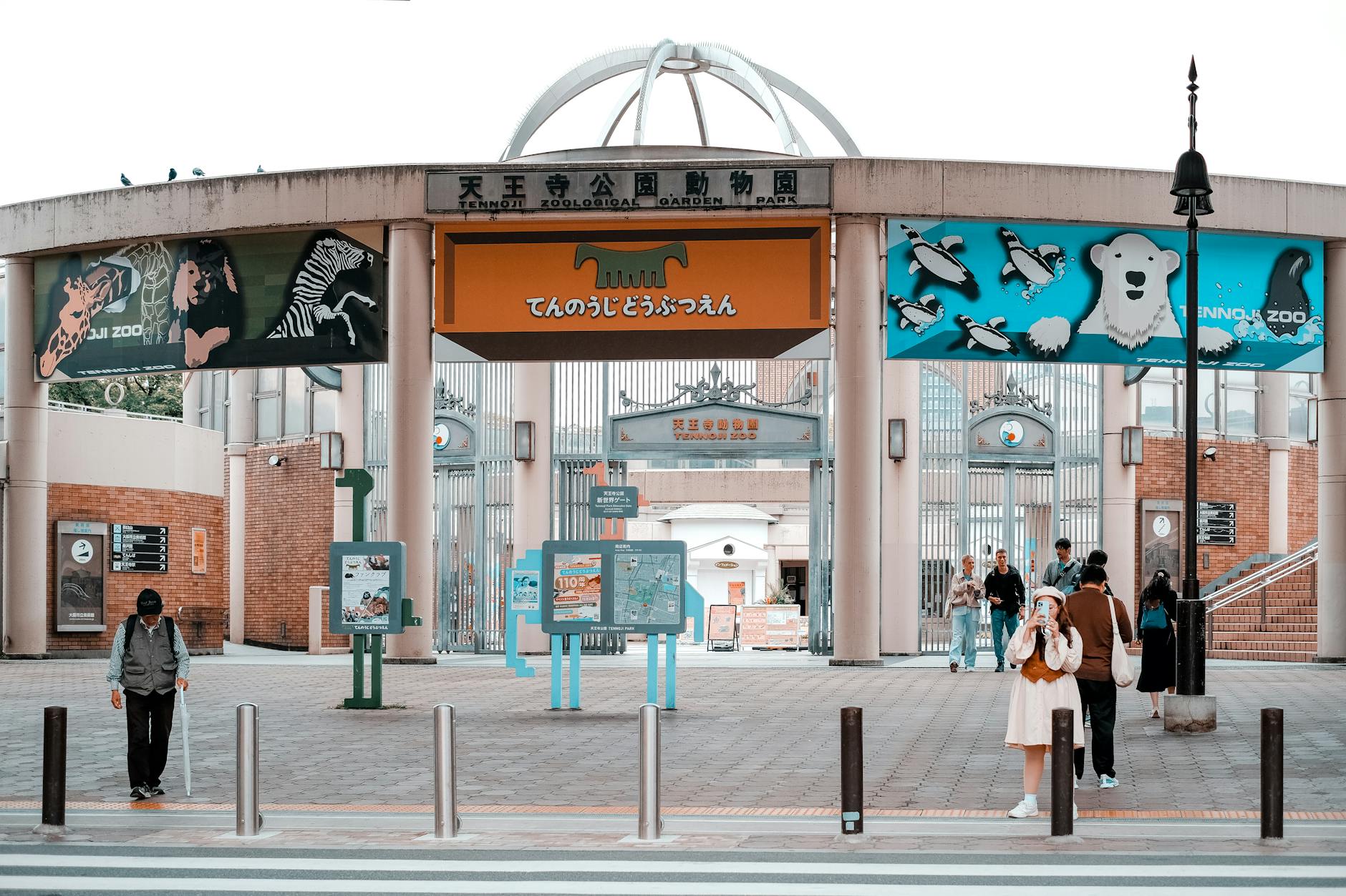 People walking in front of the entrance to Tennoji Zoo in Osaka, showcasing banners and zoo attractions.