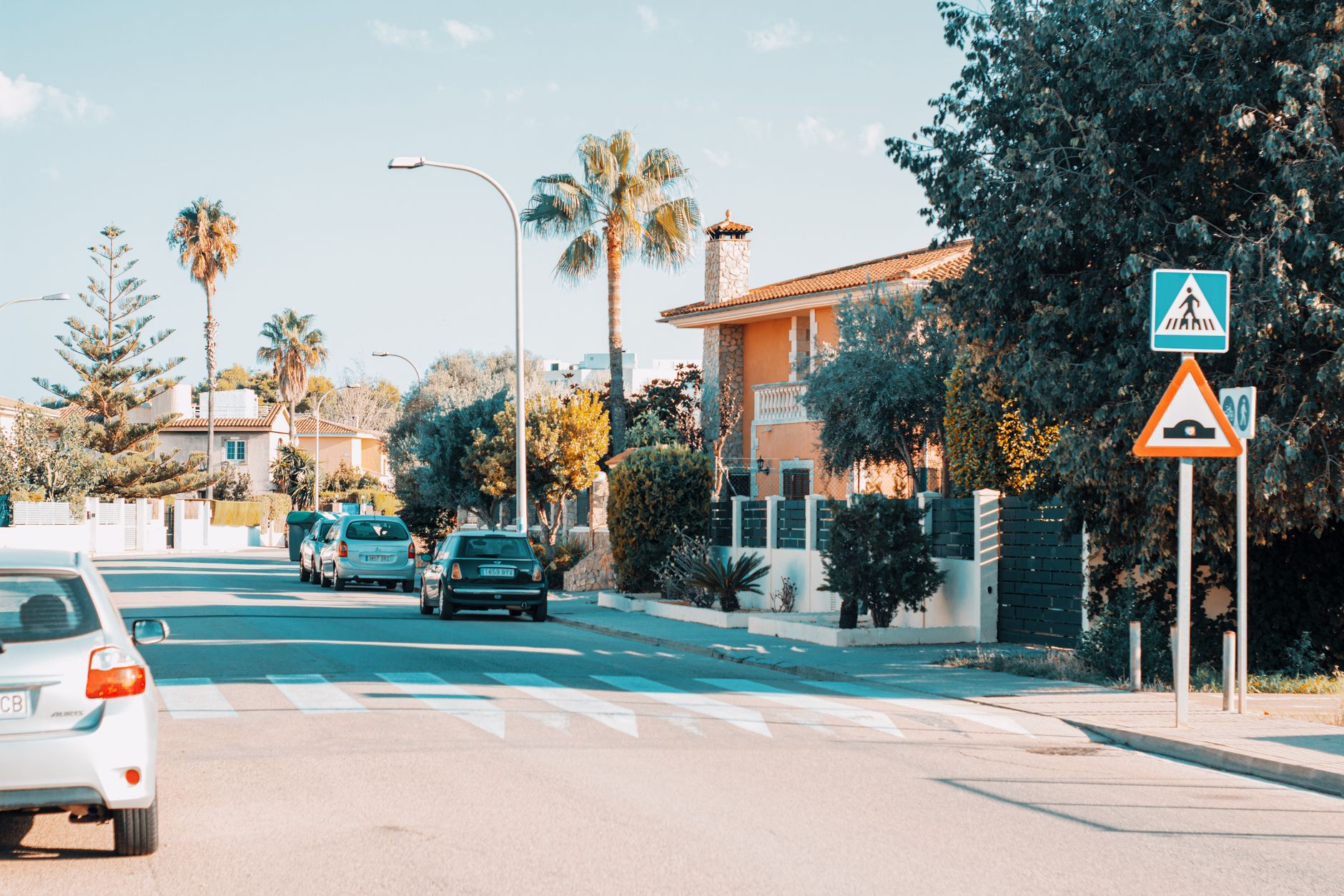 Sunny suburban street with palm trees and cars in Palma de Mallorca, Spain, showcasing Mediterranean architecture.