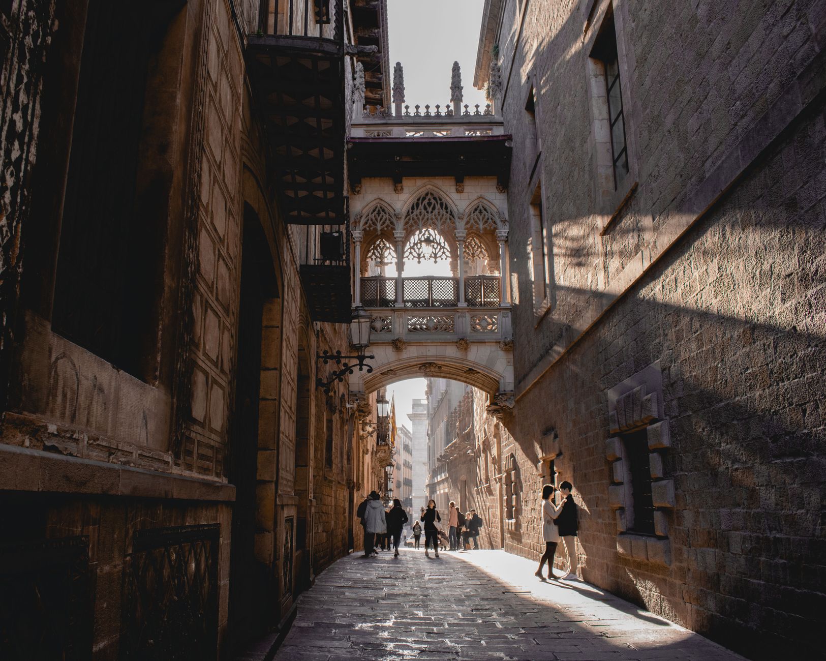 People walking under Pont del Bisbe in Barcelona&rsquo;s Gothic Quarter.