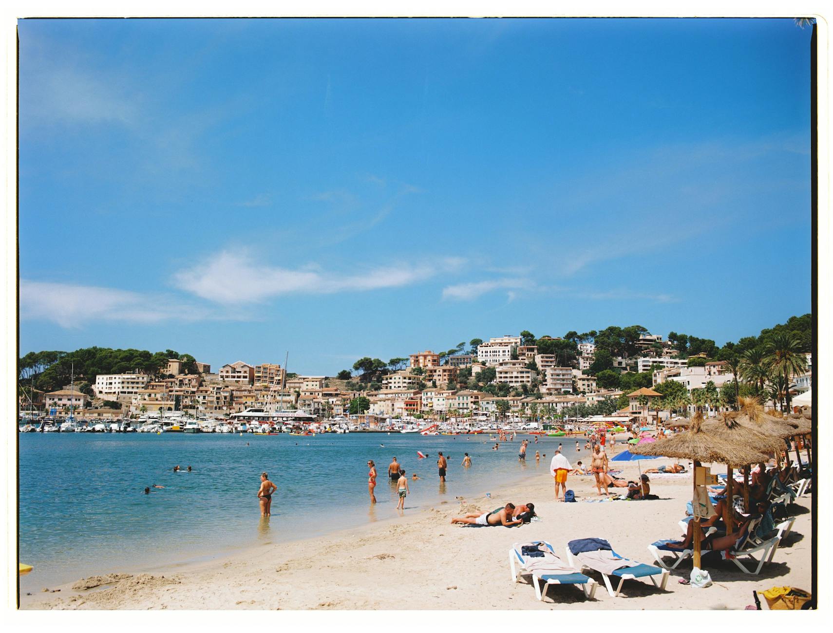 Vibrant summer day at the beach in Port de Sóller, Mallorca with people enjoying the sun and sea.