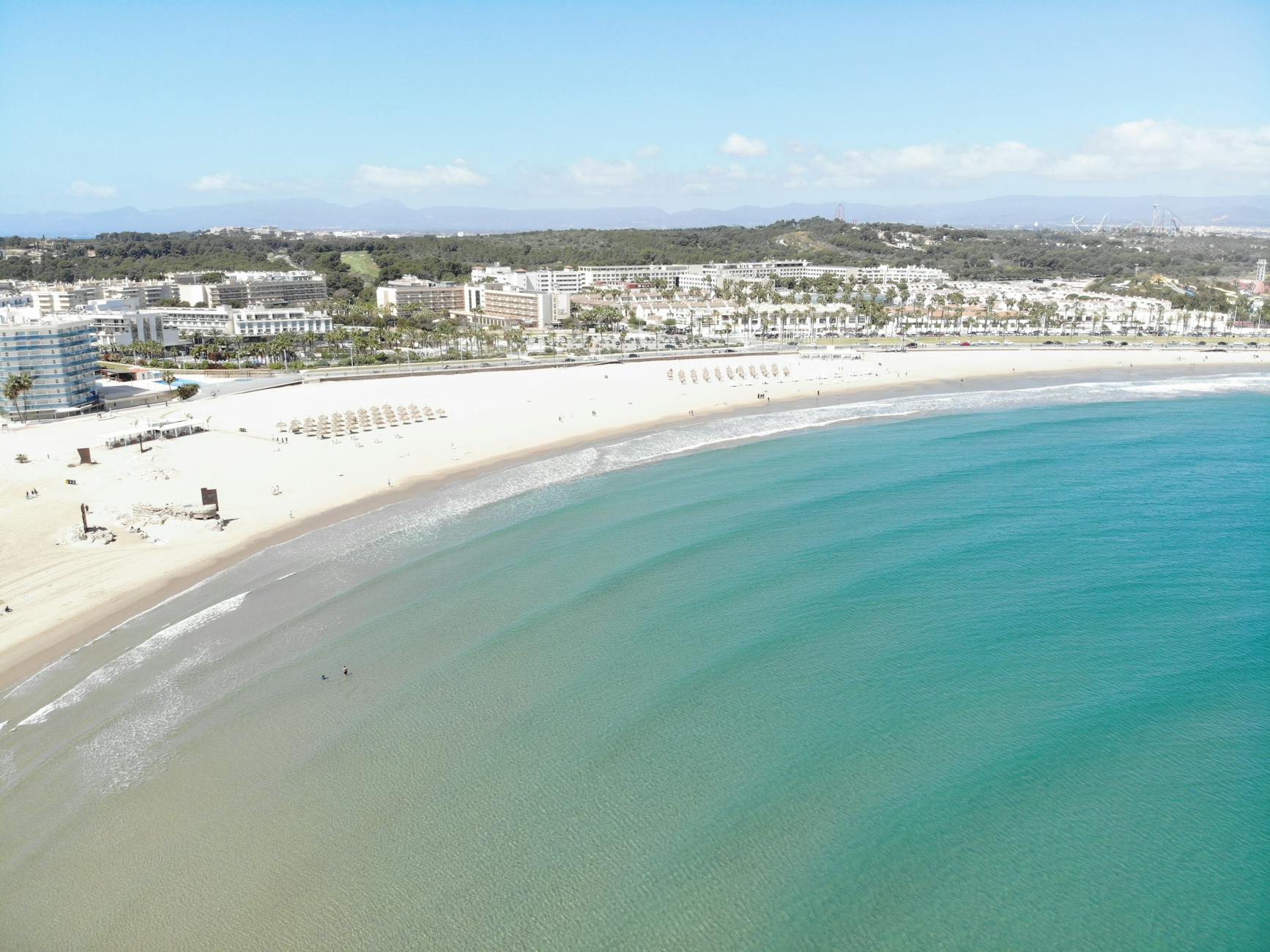 Stunning aerial view of a beachfront resort in Catalonia, showcasing clear waters and sandy shores.