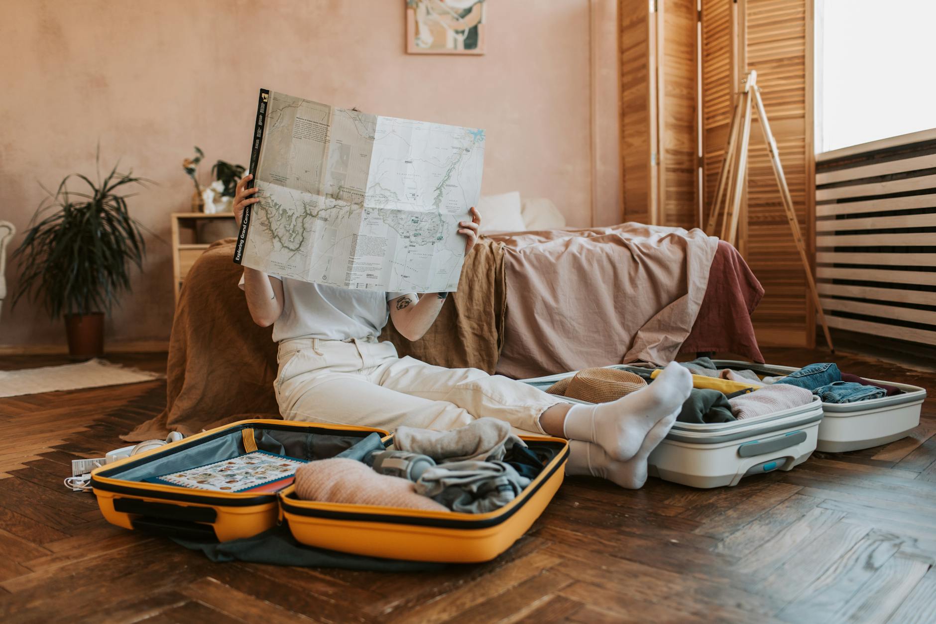 Person packing suitcases with a map in a cozy bedroom, preparing for a journey.