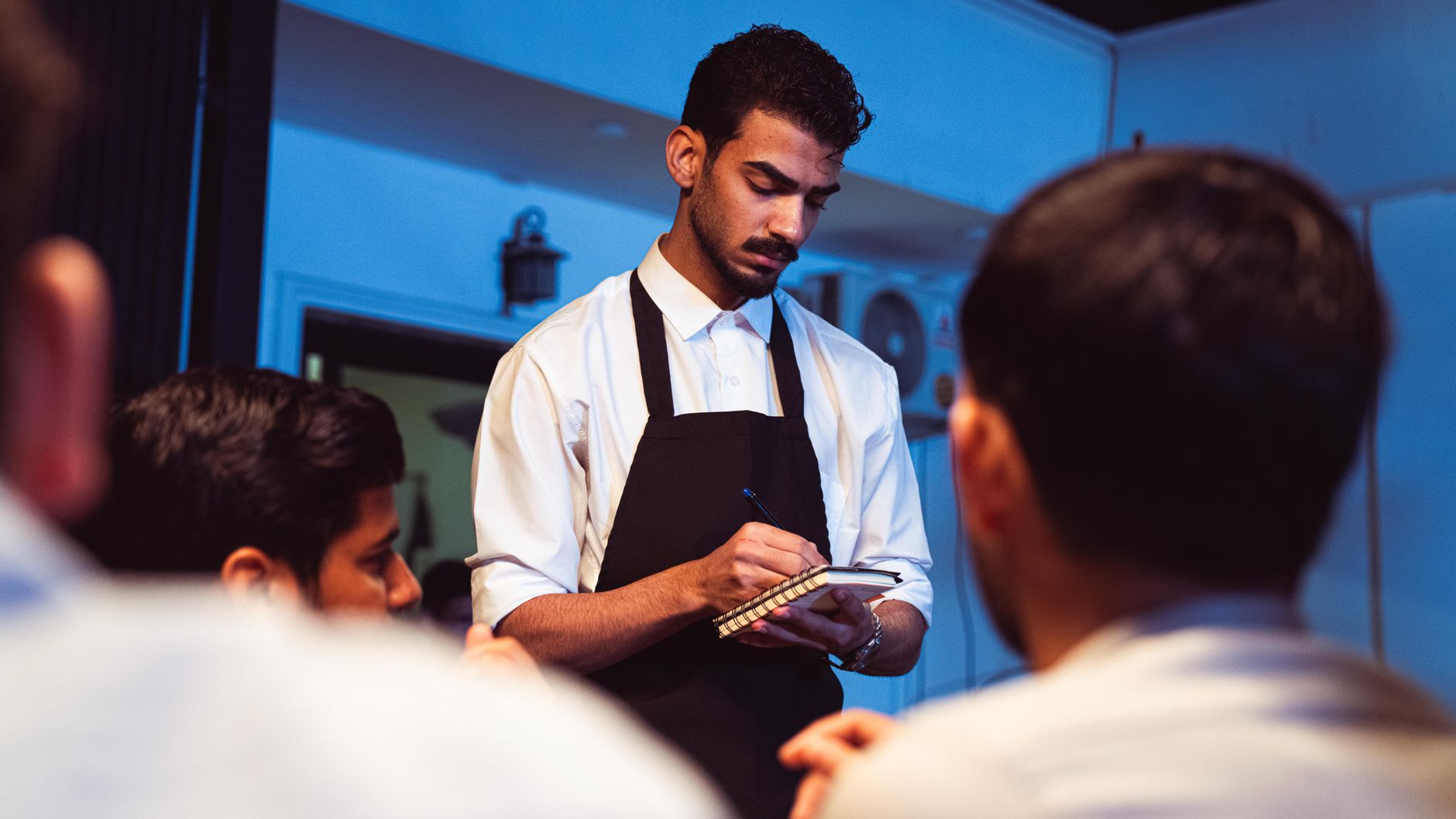 Attentive waiter writing down a customer&rsquo;s order in a cozy indoor restaurant.