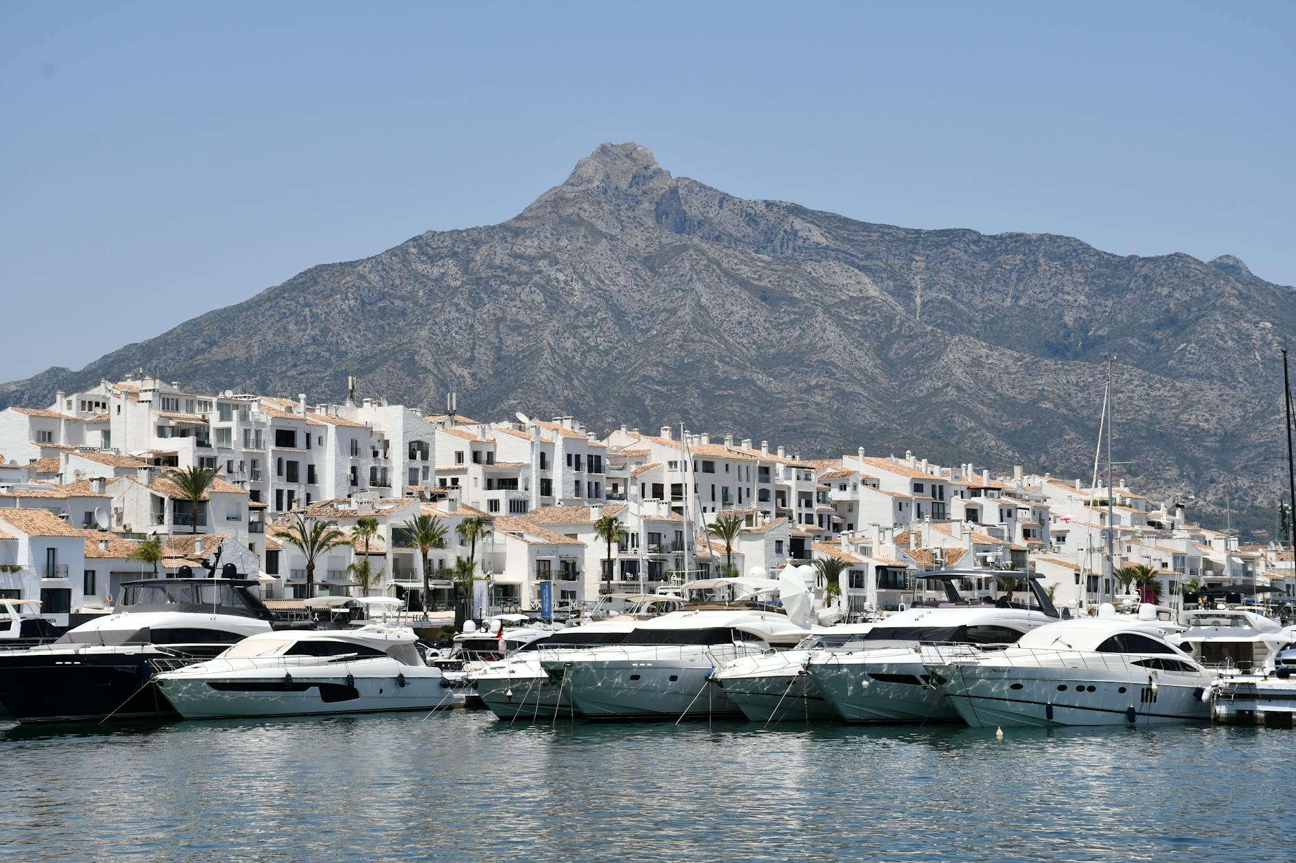 Luxury yachts docked at Puerto Banus with a stunning mountain backdrop, capturing the essence of wealth and tourism.