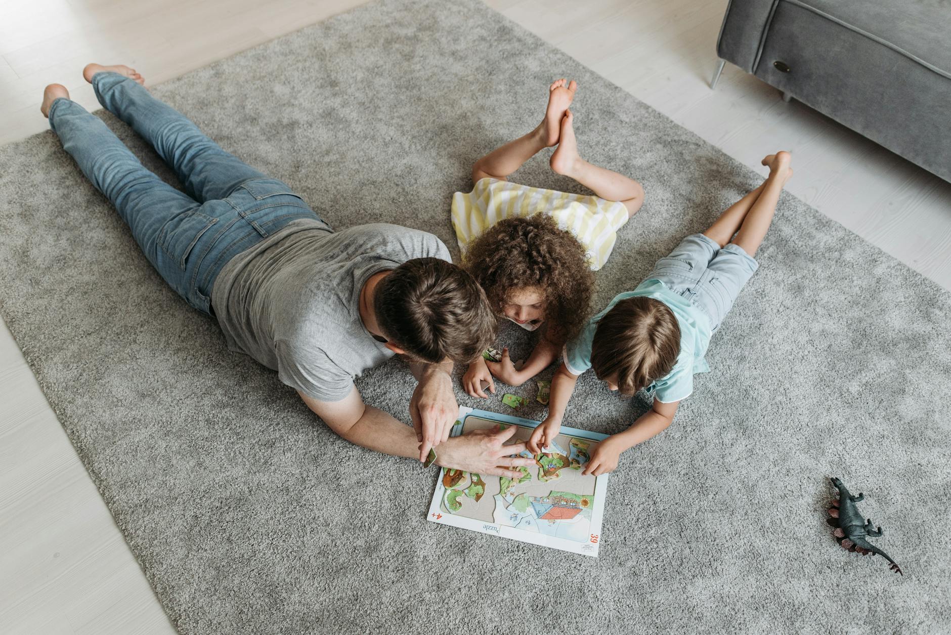 Father and kids enjoy quality time solving a puzzle together on a living room rug.