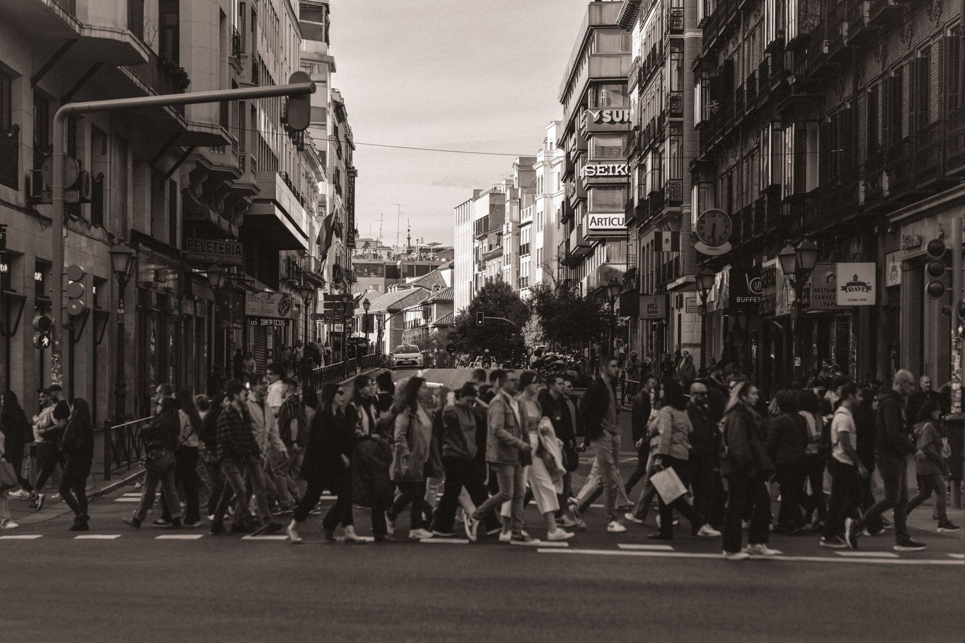 A bustling city street in Madrid with people crossing. Urban lifestyle captured in sepia tones.