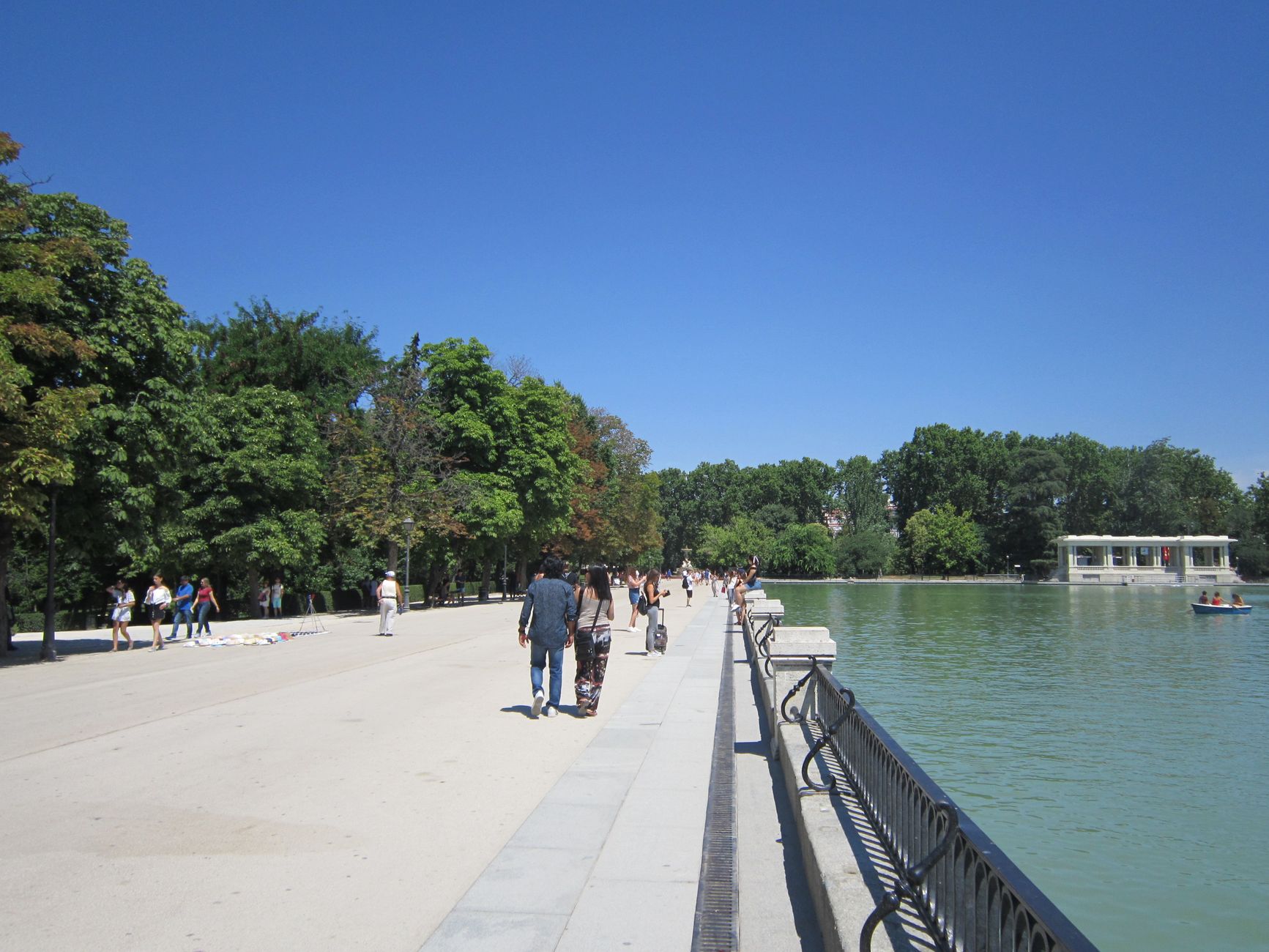 People enjoying a sunny stroll by the pond in Retiro Park, Madrid.