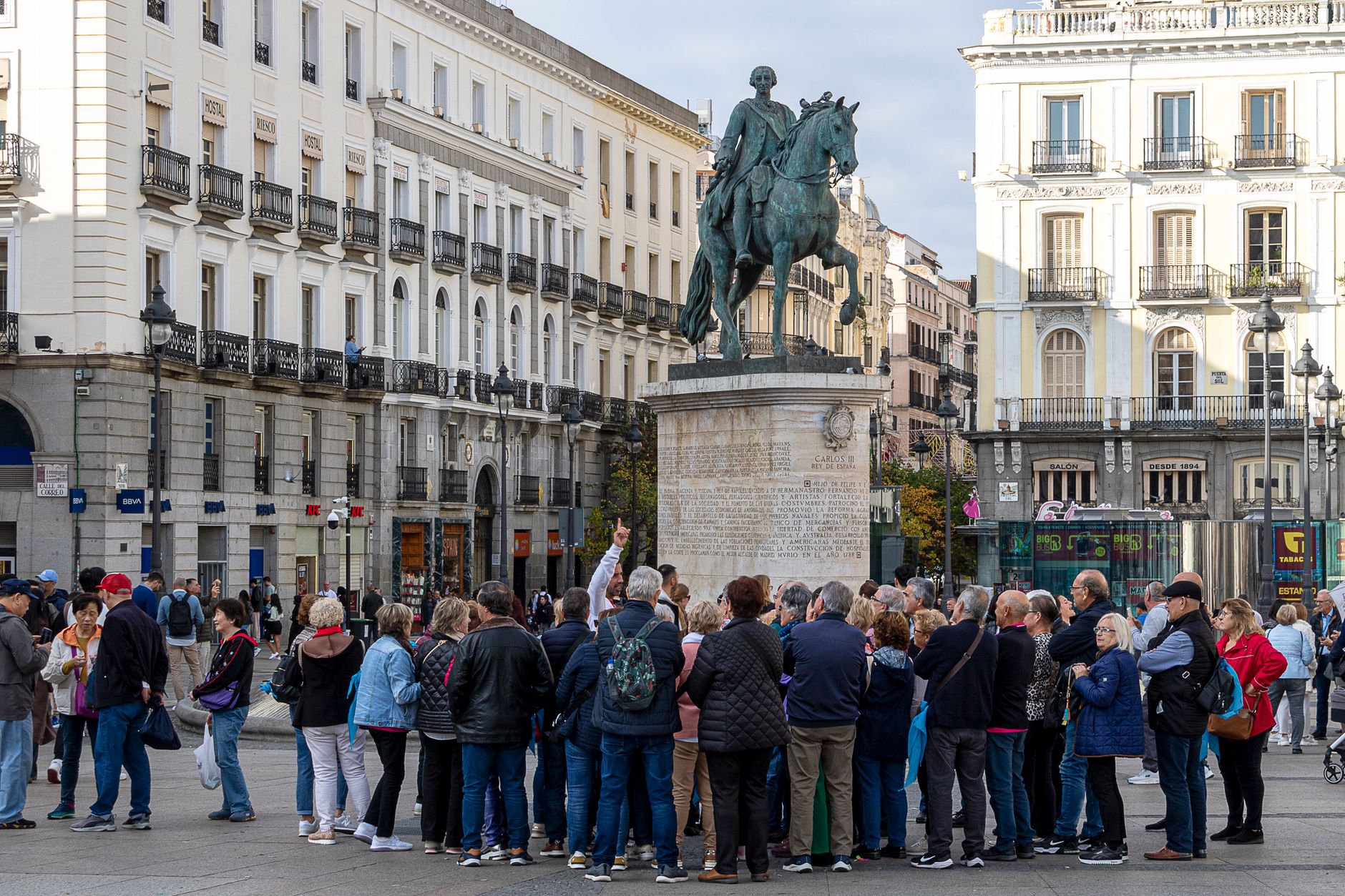 Tourists gather around the equestrian statue in Madrid&rsquo;s Puerta del Sol. Vibrant urban scene.