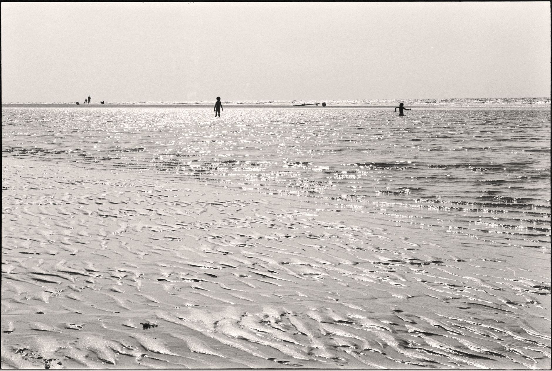 Black and white photo of children playing in shallow ocean waters on a sunny day.
