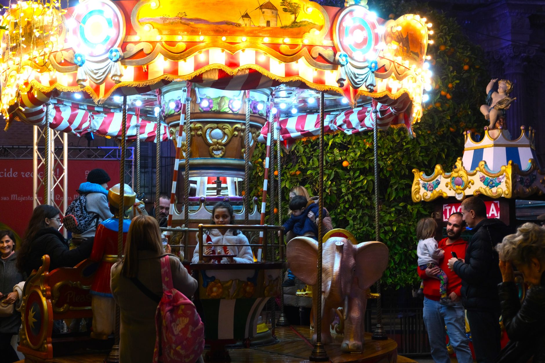 A vibrant funfair carousel lit up at night in Murcia, Spain, featuring joyful families.