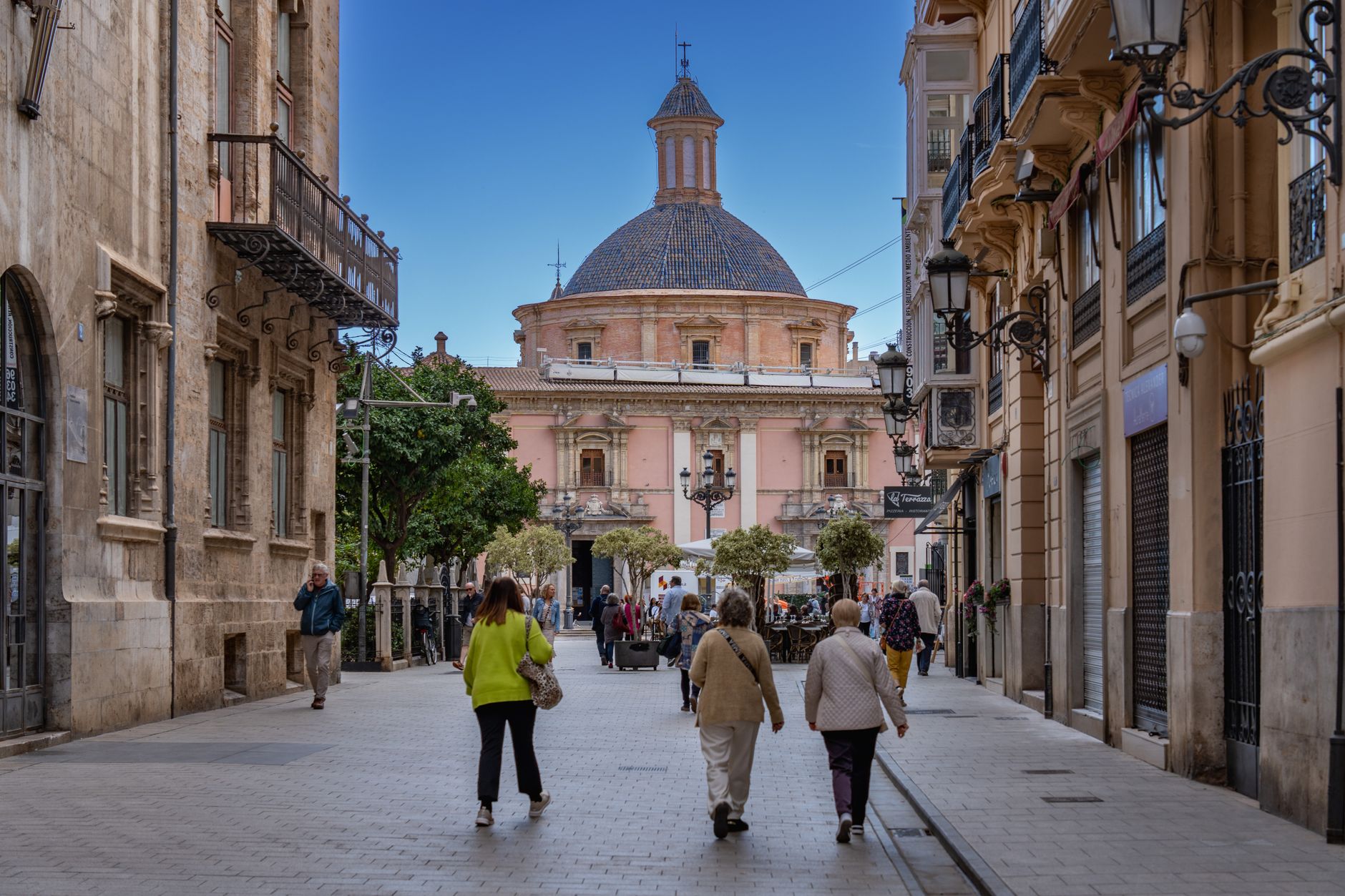 Charming street in Valencia with historical architecture and people enjoying the day.