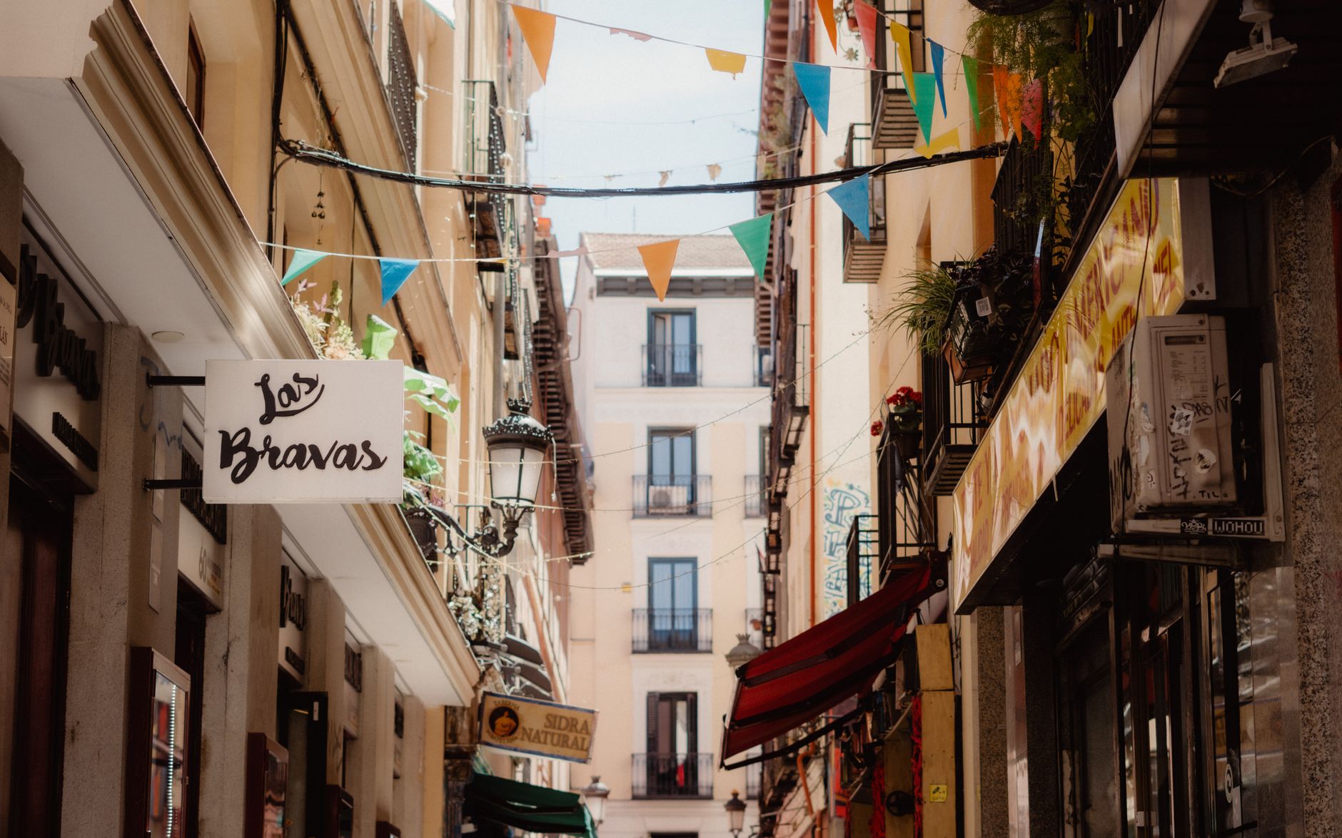 Charming Madrid street with vibrant flags and traditional storefronts.