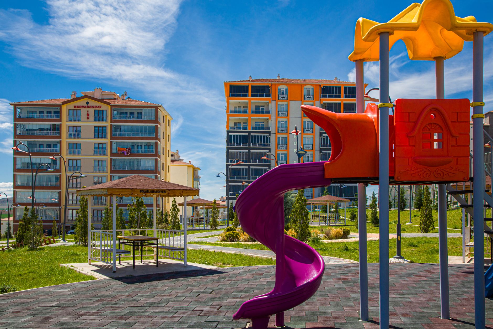 Vibrant playground with a slide in a green urban park amidst modern buildings.