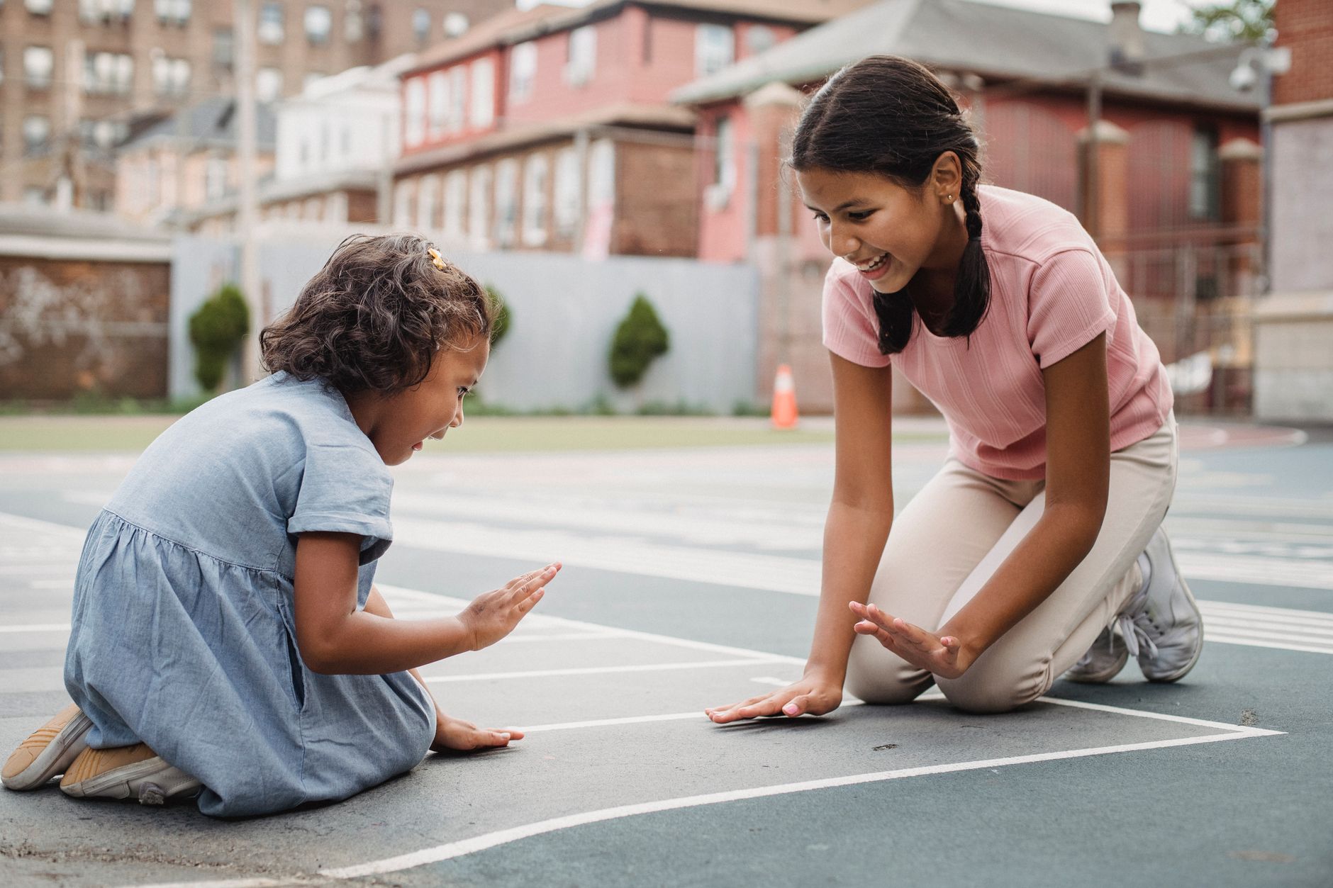 Two girls joyfully play a hand game on an urban playground, showcasing friendship and fun.