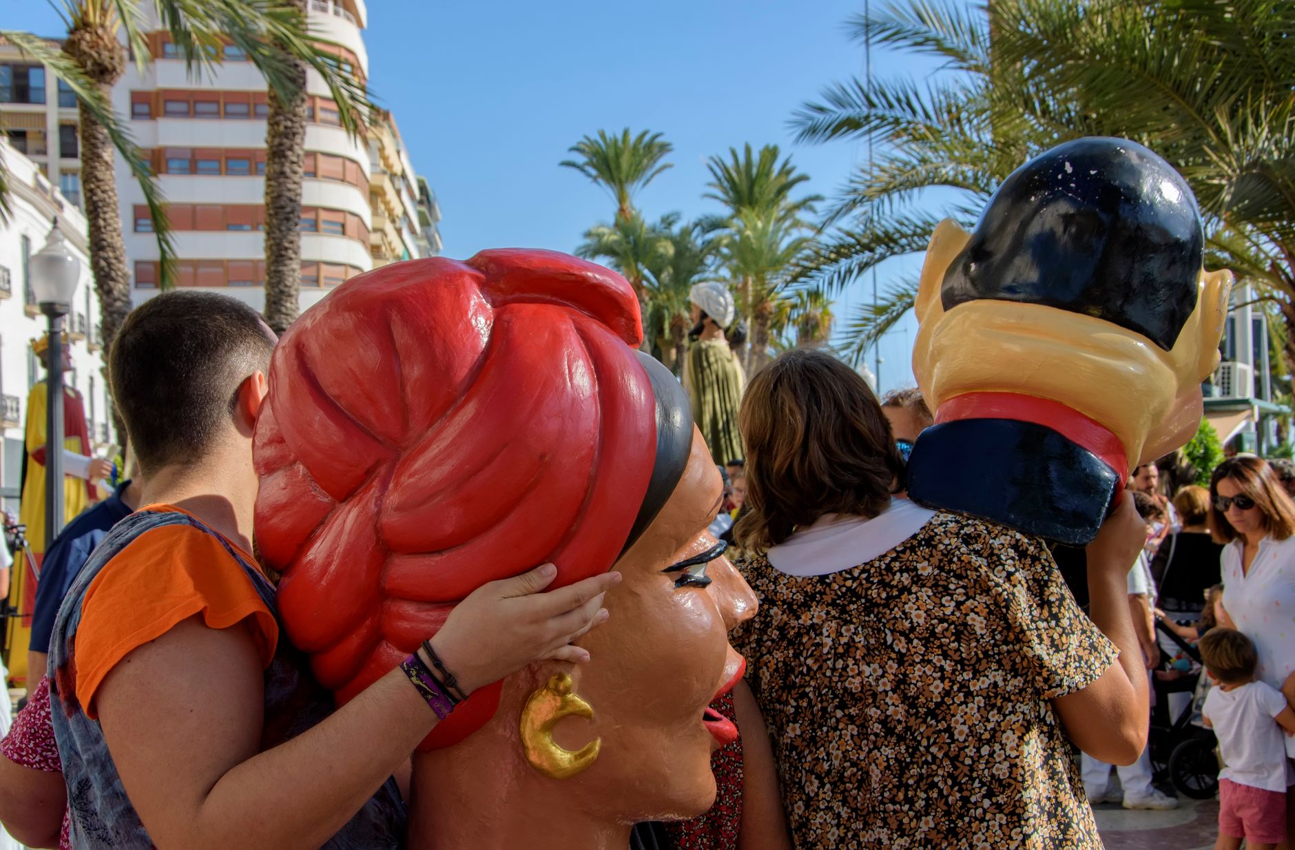 Festive street parade with giant heads during daytime in Alicante, Spain.