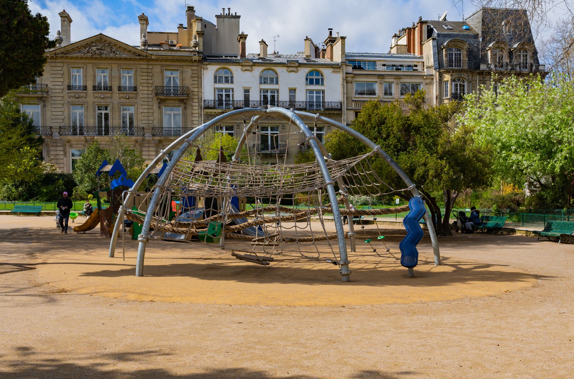 A modern playground with climbing structures in a sunny urban park.