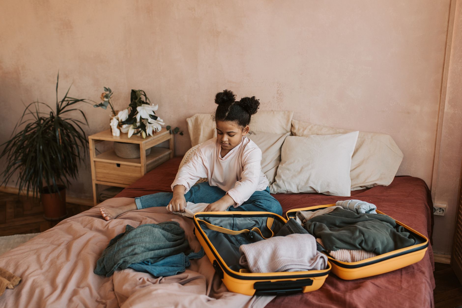 A young girl packing a suitcase on a bed in a cozy bedroom setting. Perfect for travel and family themes.