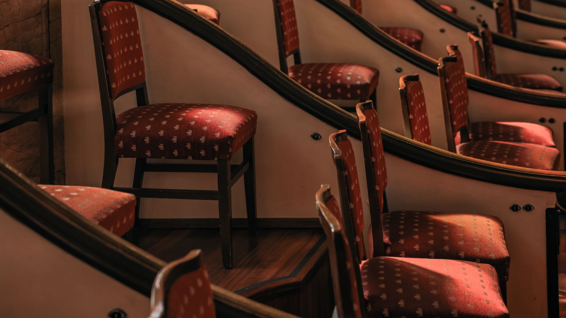 Curved rows of elegant red theater seats in a sunlit Barcelona auditorium.