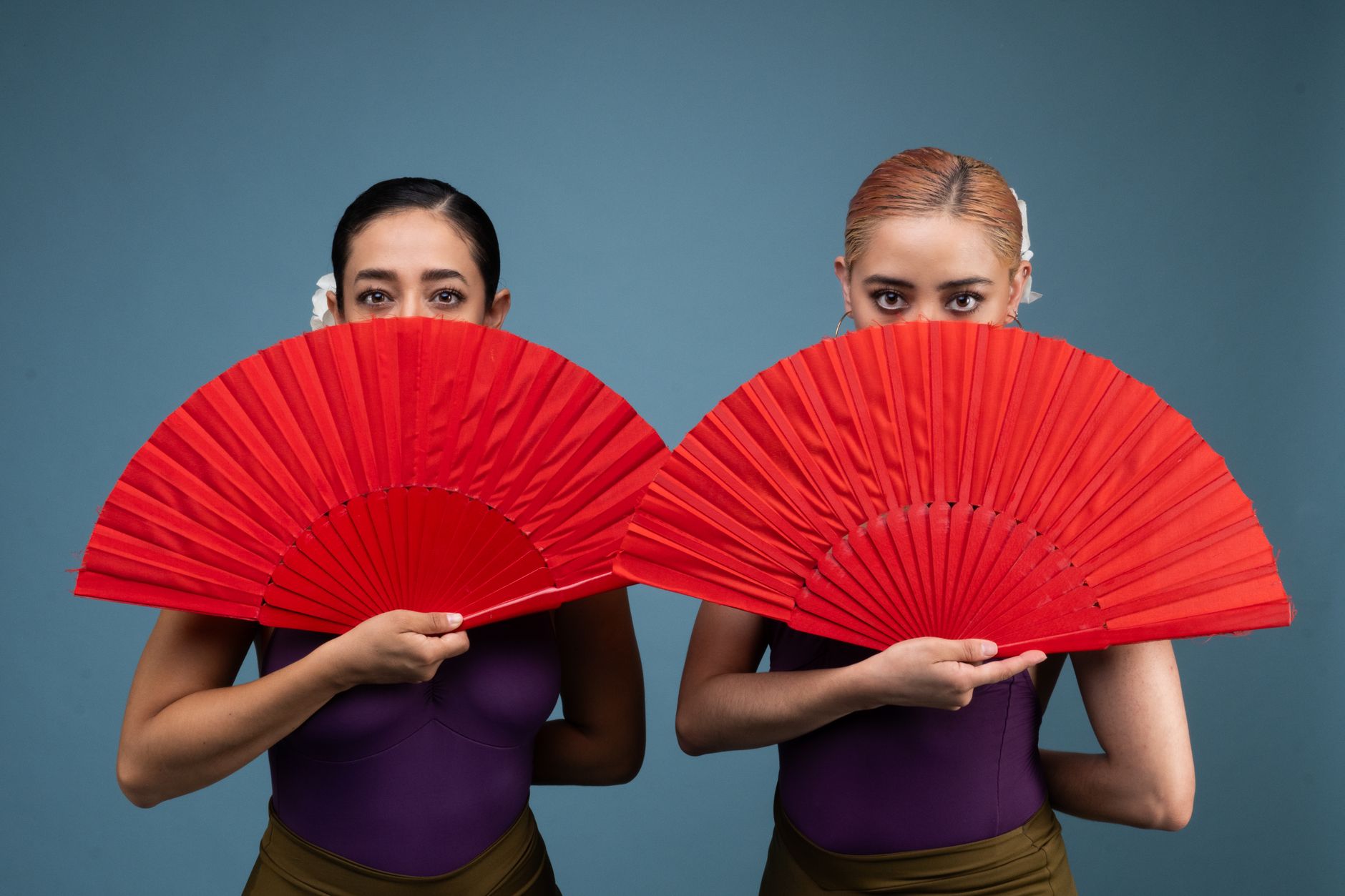 Two female dancers in vibrant attire hold red fans, showcasing Mexican culture.