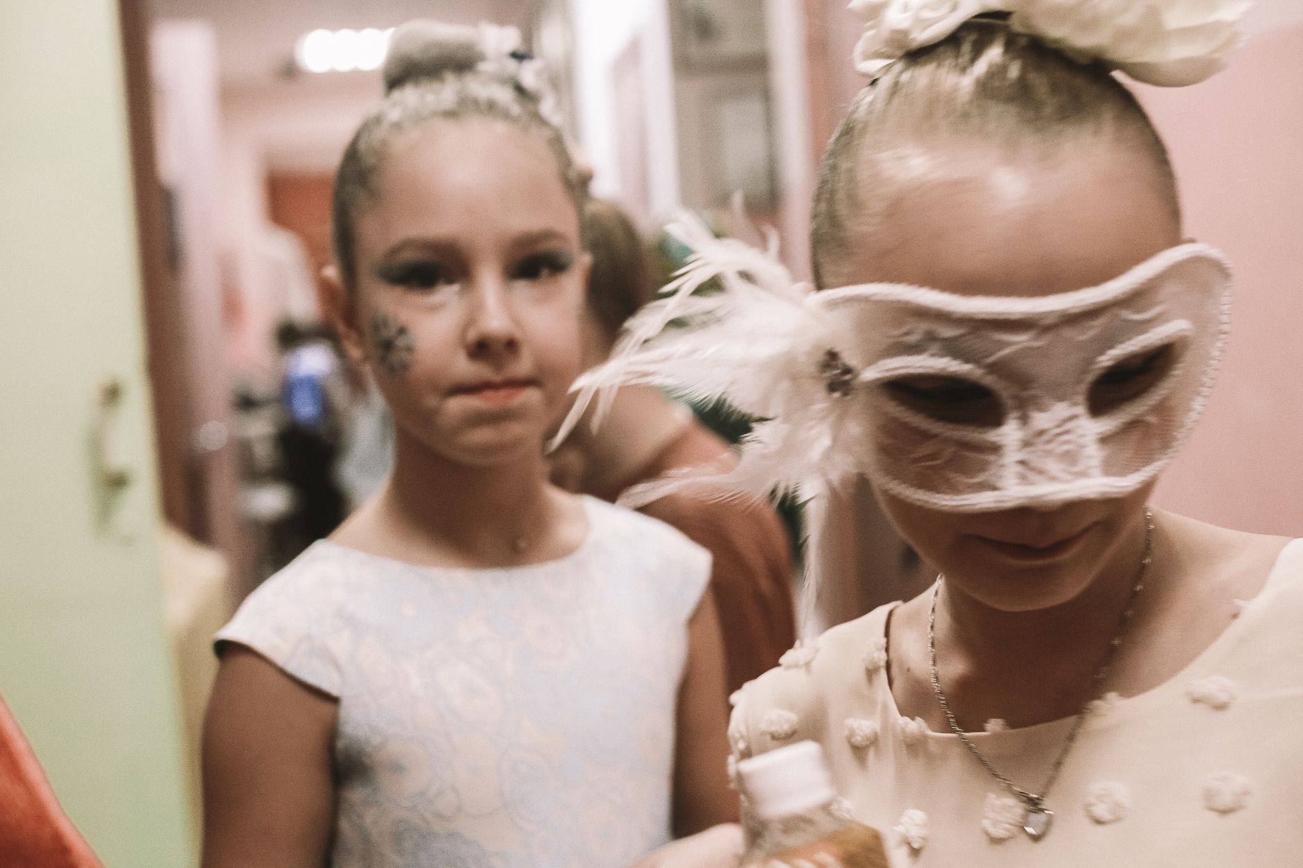 Two young girls dressed in festival attire and masks, preparing for a celebration indoors.